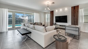A modern living room with a large sofa, a coffee table, and a TV. There is a balcony with a pool view. - Solara Resort 9 Bedroom 6 Bathroom Resort 9024srl (Kissimmee)