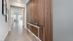 A hallway with a wooden panel wall, a glass console table, and a tiled floor. - Solara Resort 9 Bedroom 6 Bathroom Resort 9024srl (Kissimmee)