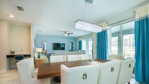 A dining area with a wooden table and white chairs, a chandelier, and a ceiling fan.