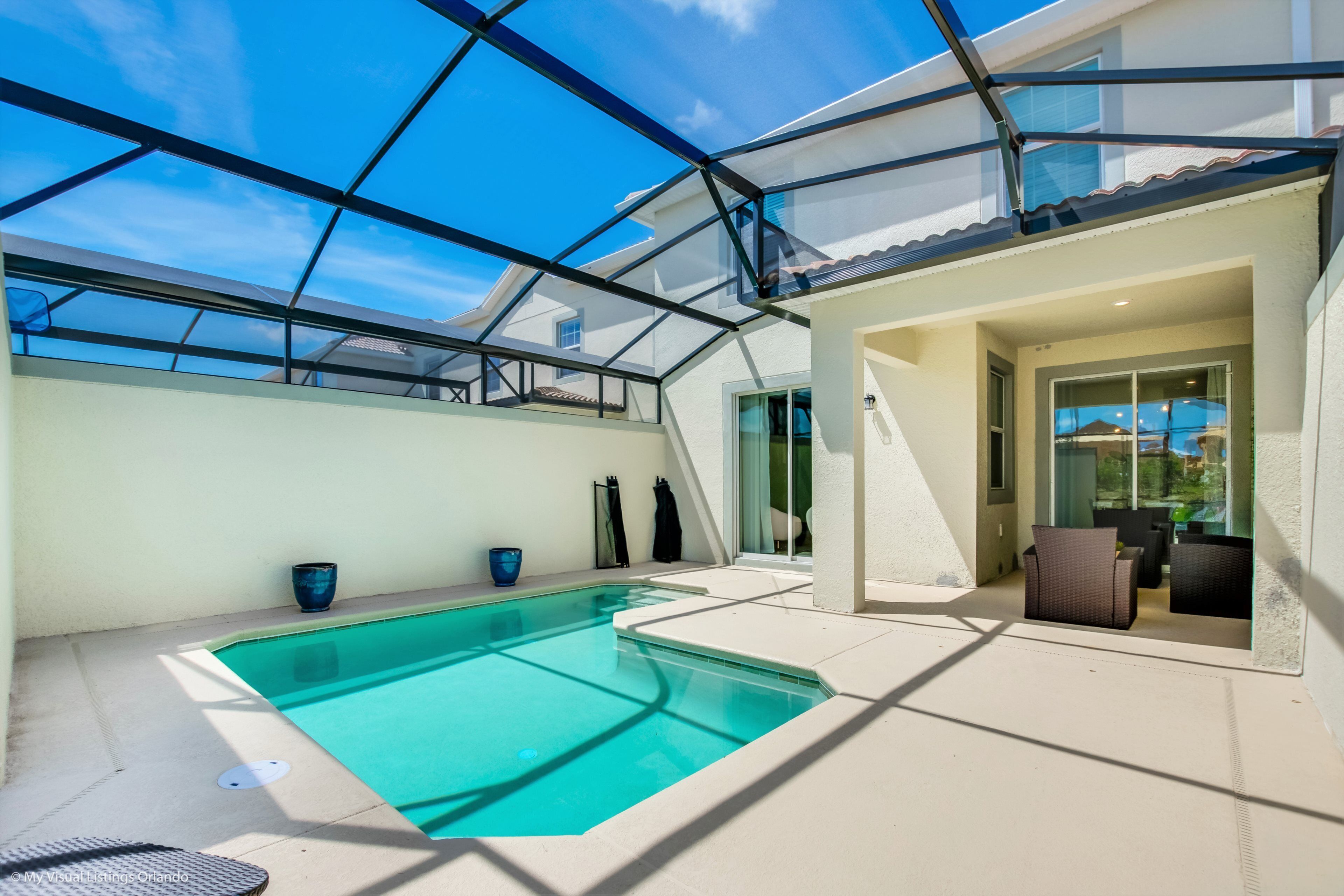 A modern pool area with a glass ceiling, clear blue sky, and a patio with seating.