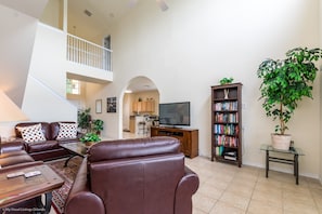 A spacious living room with a brown leather sofa, a flat-screen TV, a bookshelf, and a large potted plant. - 526wp 5 bed 4 Bathroom Overlooking Amazing View (Davenport)