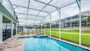 Ein Schwimmbecken mit Glasumrandung, umgeben von einer Ziegelterrasse und einer Rasenfläche.