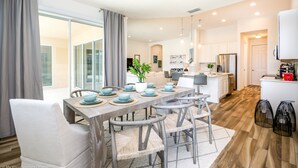 A modern kitchen with white cabinets, a stainless steel refrigerator, and a dining area with a wooden table and chairs.