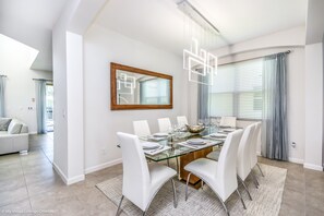A modern dining room with a glass table, white chairs, and a wooden-framed mirror. - 5196oa Luxury 6 Bedroom 5.5 Bath Home (Davenport)