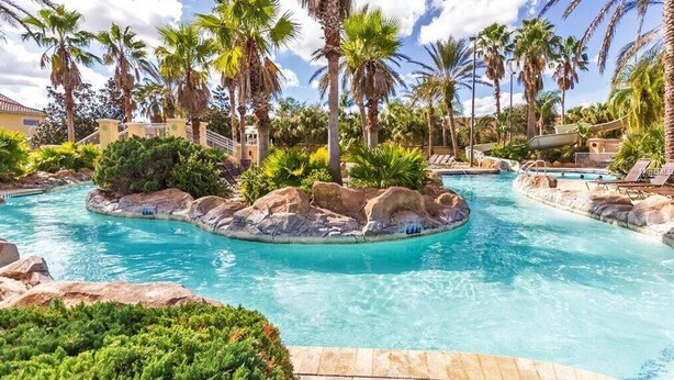 A pool area with palm trees, a rock island, and lounge chairs. - Clabria Villa Regal Palms (Davenport)