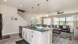 A modern kitchen with white cabinets, a granite countertop, and a blue sink. There is a dining area with a gray sofa and patterned rug. - 5153ad Amazing Compass Baytown Home Sleeps 10 (Kissimmee)