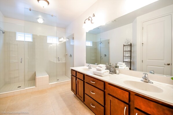 A modern bathroom with a glass-enclosed shower, a large mirror, and wooden cabinetry. - 7770ll Ultimate Reunion Home (Kissimmee)