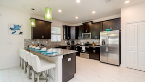 A modern kitchen with dark cabinets, stainless steel appliances, and a central island with bar stools. - 9037hs 6 Bedroom 6 Bathroom Champions Gate Villa (Davenport)