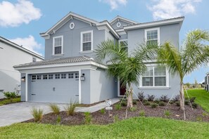 A two-story house with a garage, a well-maintained lawn, and a small tree in the front yard. - 1571pw Amazing Champions Gate 6 Bedroom 6 Bed (Davenport)