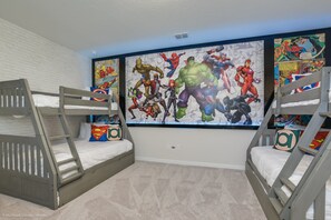 Une chambre d’enfant avec des lits superposés, une grande fresque murale sur le thème des super-héros et un mur en briques blanches.