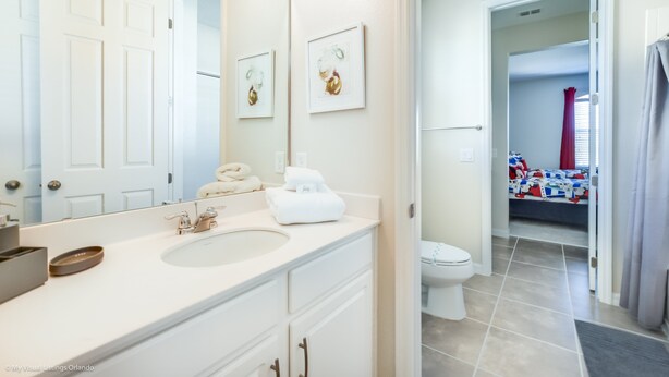 A bathroom with a white sink, a mirror, and a toilet. There are towels on the counter and a shower curtain in the background. - 1720sppp Amazing 7 Bedroom 6 bed Resort Villa (Kissimmee)