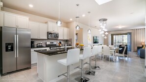 Una cocina moderna con electrodomésticos de acero inoxidable, una isla central con taburetes de bar e iluminación colgante.