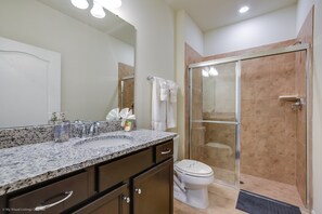 Une salle de bain avec un comptoir en granit, des toilettes, une douche en verre et une porte blanche.