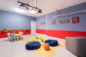 Une salle de jeux avec un sol à carreaux, des fauteuils en forme de poire, un ballon de basket et des décorations murales colorées.