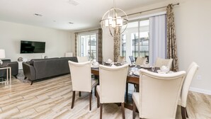 A modern dining area with a chandelier, a dining table set for four, and a sofa in the background. - 4720shd Ultimate New 6 Bedroom Storey Lake Home (Kissimmee)