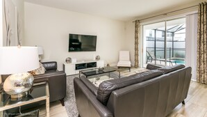 A modern living room with a sofa, coffee table, and TV. There is a balcony with a glass door and curtains. - 4720shd Ultimate New 6 Bedroom Storey Lake Home (Kissimmee)