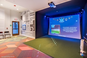 Quarto com uma tela grande exibindo uma partida esportiva, piso com padrão geométrico e parede com diversos gráficos relacionados a esportes.