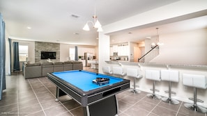 Uma sala de estar moderna com mesa de bilhar, sofá e área de cozinha.