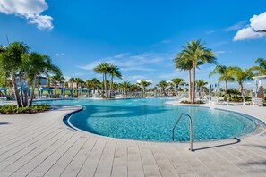 Ein großer, klarer Pool mit gewölbter Kante, umgeben von Palmen und Liegestühlen.