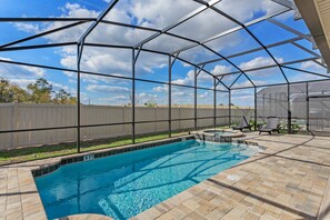Ein überdachter Pool im Freien mit einer Terrassenfläche, einem Zaun und blauem Himmel.