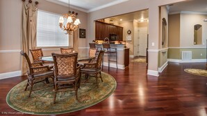 A dining area with a round table and six chairs, a chandelier, and a view into the kitchen. - 7704ll Ultimate Reunion Home (Kissimmee)