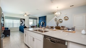 A modern kitchen with a dishwasher, double sink, and a dining area with a table set for two. - 910pb Luxury Furnished 5 Bedroom 5 Bathroom (Davenport)
