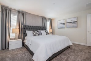 A bedroom with a tufted headboard, a white bedspread, two bedside tables with lamps, and a view of the outdoors through large windows. - Lullaby Lane Villa Storey Lake (Kissimmee)