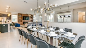 A modern dining area with a glass table set for six, surrounded by dark upholstered chairs. - 1798cvt Solara Resort 9 Bedroom 6 Bathroom Villa (Kissimmee)