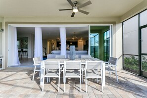 An outdoor patio with a dining table and chairs, a ceiling fan, and a view of the interior.