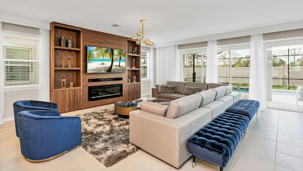 A modern living room with a large TV, a sofa, a blue chair, and a wooden entertainment unit. - 1798cvt Solara Resort 9 Bedroom 6 Bathroom Villa (Kissimmee)