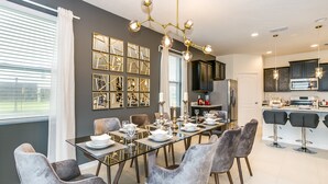 Un comedor moderno con una mesa de vidrio, sillas tapizadas en gris y una araña.
