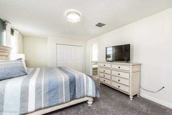 Un dormitorio con cama, cómoda, televisor y una puerta.
