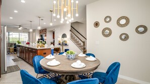 Een moderne keuken met een centraal eiland, blauwe stoelen rond een houten eettafel en decoratieve spiegels aan de muur.