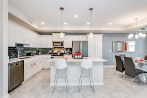 A modern kitchen with white cabinets, a central island with bar stools, and a dining area with a gray wall and a large mirror. - 3111u307 Amazing Story Lake Brand New Condo (Kissimmee)