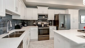 A modern kitchen with white cabinets, a stainless steel refrigerator, a microwave, a stove, and a sink. - 3111u307 Amazing Story Lake Brand New Condo (Kissimmee)