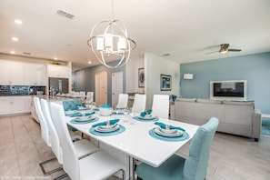 A modern kitchen with white cabinets, a dining area with a white table set for six, teal chairs, and a ceiling fan. - Flange Drive Champions Gate 1564 (Davenport)
