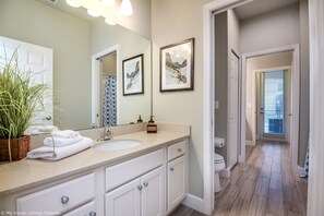 Une salle de bain avec un grand miroir, deux œuvres d’art encadrées, un lavabo et des toilettes.