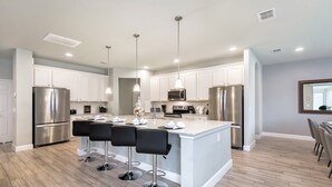 A modern kitchen with stainless steel appliances, white cabinetry, and a central island with bar stools. - Broad Oak Villa Solterra 3 (Davenport)