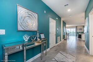 A modern hallway with teal walls, a console table with decorative items, and a view into the kitchen area. - Interlocking Drive Villa Champions Gate (Davenport)