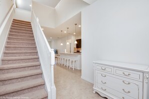 A staircase leading to a kitchen area with white bar stools and a white dresser. - 1804gobi Amazing 7 Bedroom 5 Bathroom Windsor (Kissimmee)