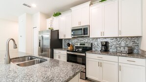 Una cocina moderna con armarios blancos, encimeras de granito, electrodomésticos de acero inoxidable y una salpicadera con un diseño de mosaico.