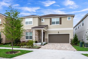 A two-story house with a stone facade, a tiled roof, and a front garage. - 1780spp New 7 Bedroom 5 Bathroom Solara Villa (Kissimmee)