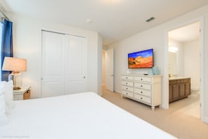 A hotel room with a bed, a dresser, a television, and a bathroom visible through an open door. - Falls Drive Reunion (Kissimmee)