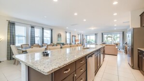 A spacious kitchen with a large island, modern appliances, and ample natural light from large windows. - Falls Drive Reunion (Kissimmee)