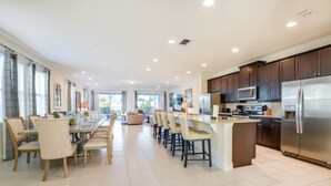 A spacious kitchen with dark wooden cabinets, stainless steel appliances, and a large island with bar stools. - Falls Drive Reunion (Kissimmee)