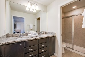 A modern bathroom with a granite countertop, dark cabinets, a large mirror, and a glass-enclosed shower. - 8887menton Ultimate 8 Bedroom 6 Bathroom Windsor (Kissimmee)