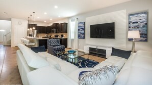 A modern living room with a white sofa, a glass coffee table, and a flat-screen TV mounted on the wall. - Bengal Court Villa Windsor At Westside Villa 1 (Kissimmee)