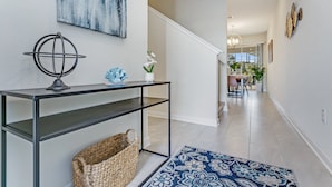 Un couloir avec une console, un panier en osier, un tapis à motifs bleus et un tableau accroché au mur.