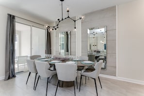 A modern dining room with a large round table, six chairs, and a chandelier.