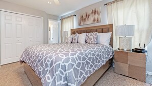 A bedroom with a large bed, a nightstand, a ceiling fan, and a door.